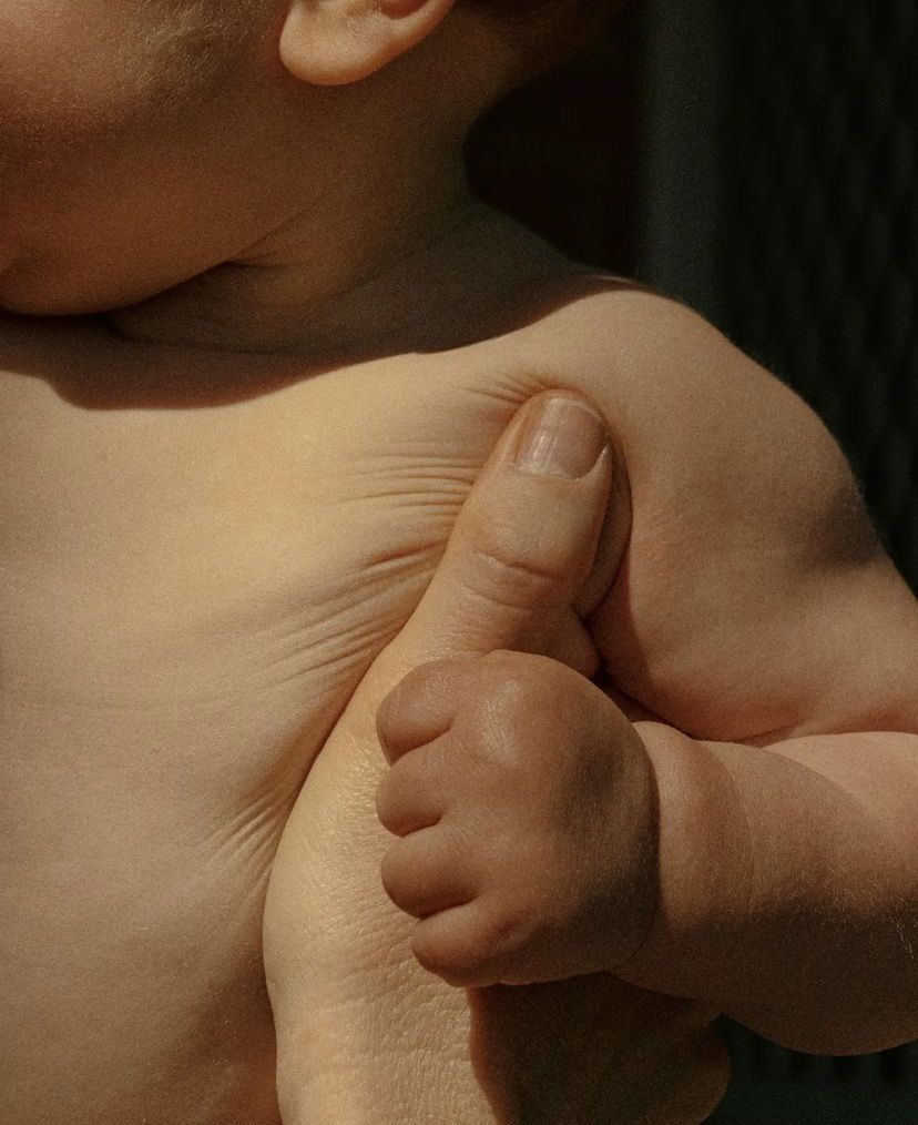 A mother's hand resting gently on a baby's foot on linen